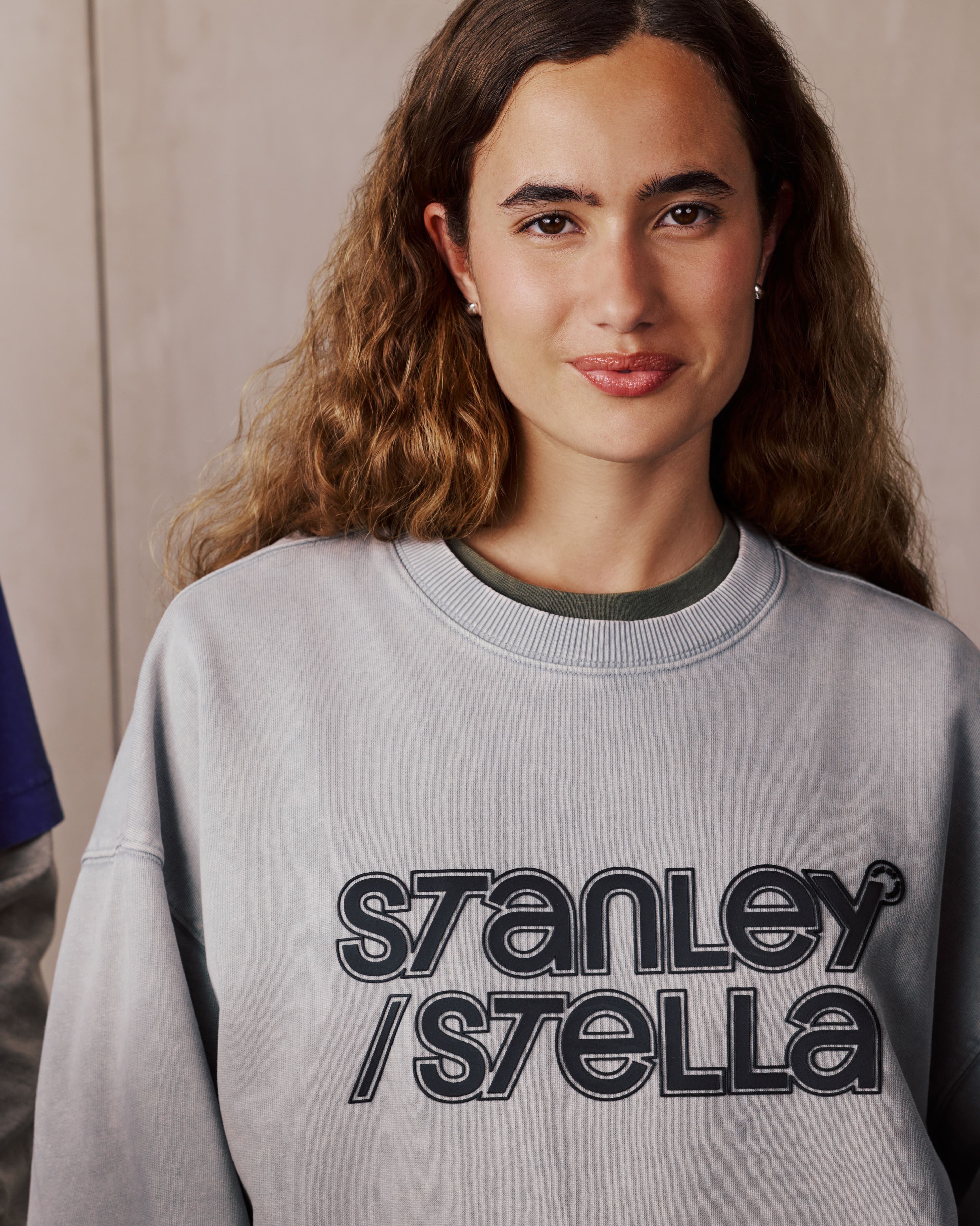 A smiling woman wears a grey sweatshirt with "STANLEY / STELLA" in black letters.